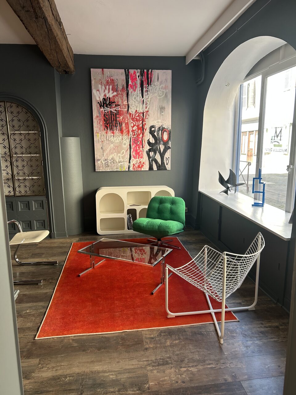Salon d'exposition avec toile street-art de DONOMIQ, fauteuil vert et chaise design.